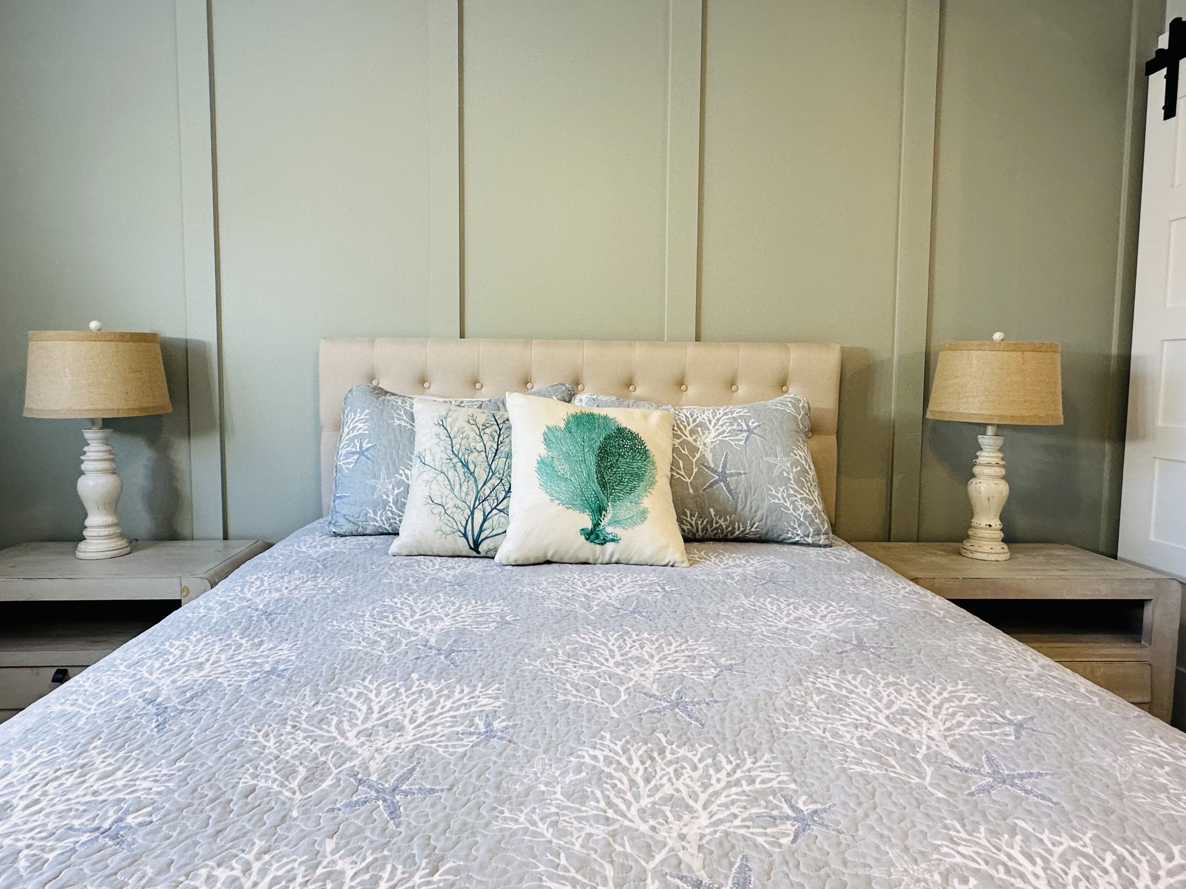 Una cama bien hecha con una colcha estampada y tres almohadones decorativos. Hay dos mesitas de noche con lámparas a cada lado de la cama.