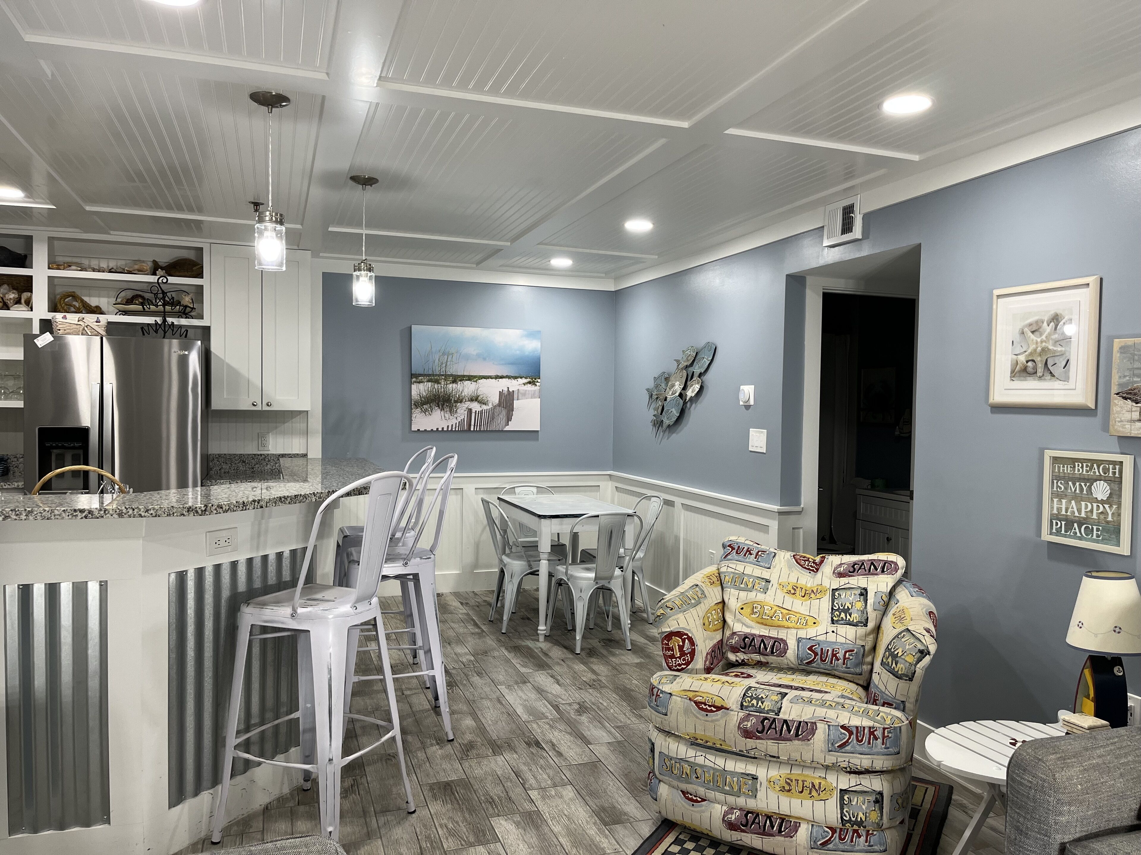Une cuisine moderne dotée d’un îlot central intégré, de tabourets de bar blancs et d’un fauteuil au thème marin.