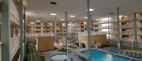 En inomhuspool med flera våningar av balkonger, ett centralt poolområde och en liten utomhusplats med sittmöbler.