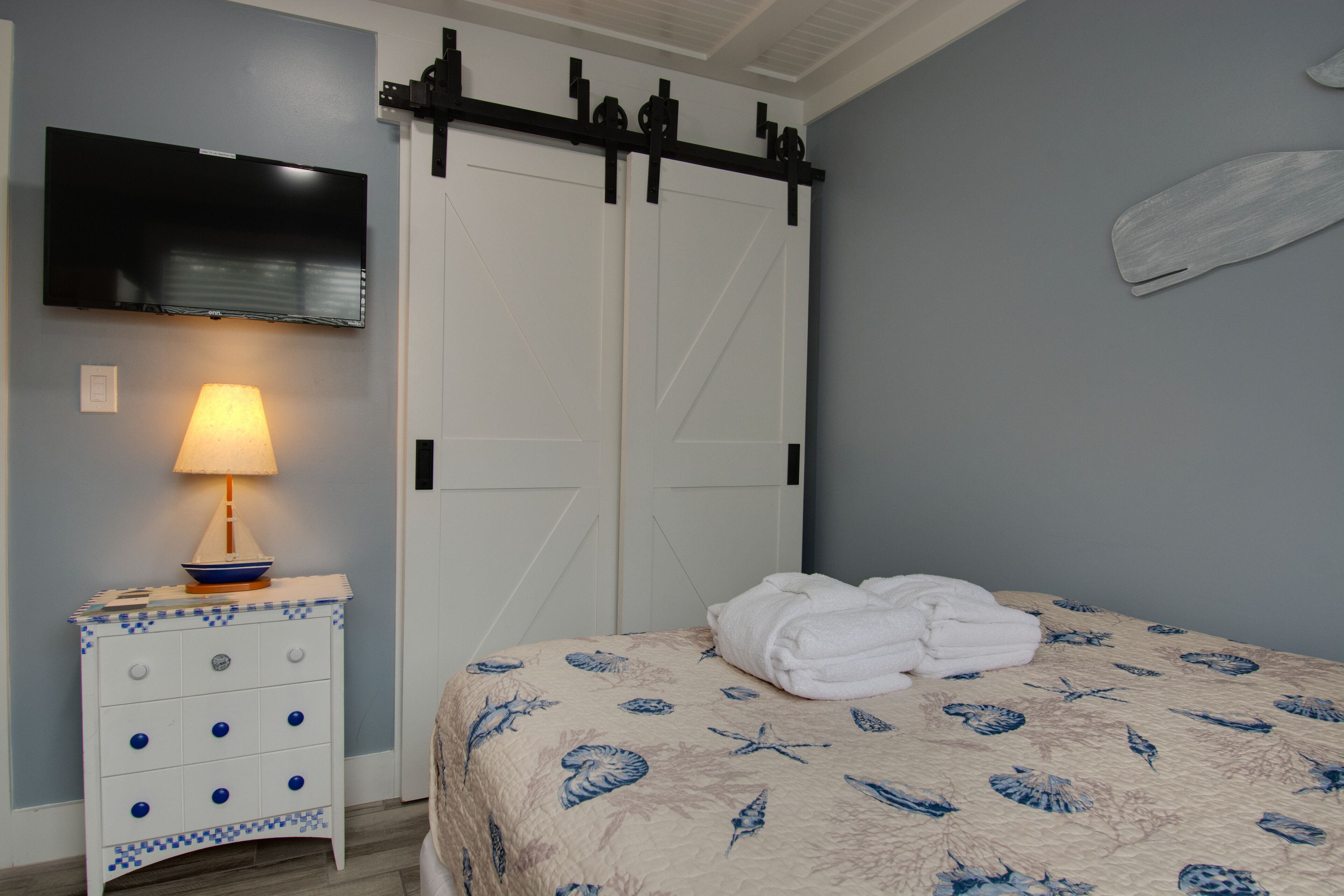 Un dormitorio con una cama, una mesita de noche con lámpara, un televisor montado en la pared y una puerta corrediza.