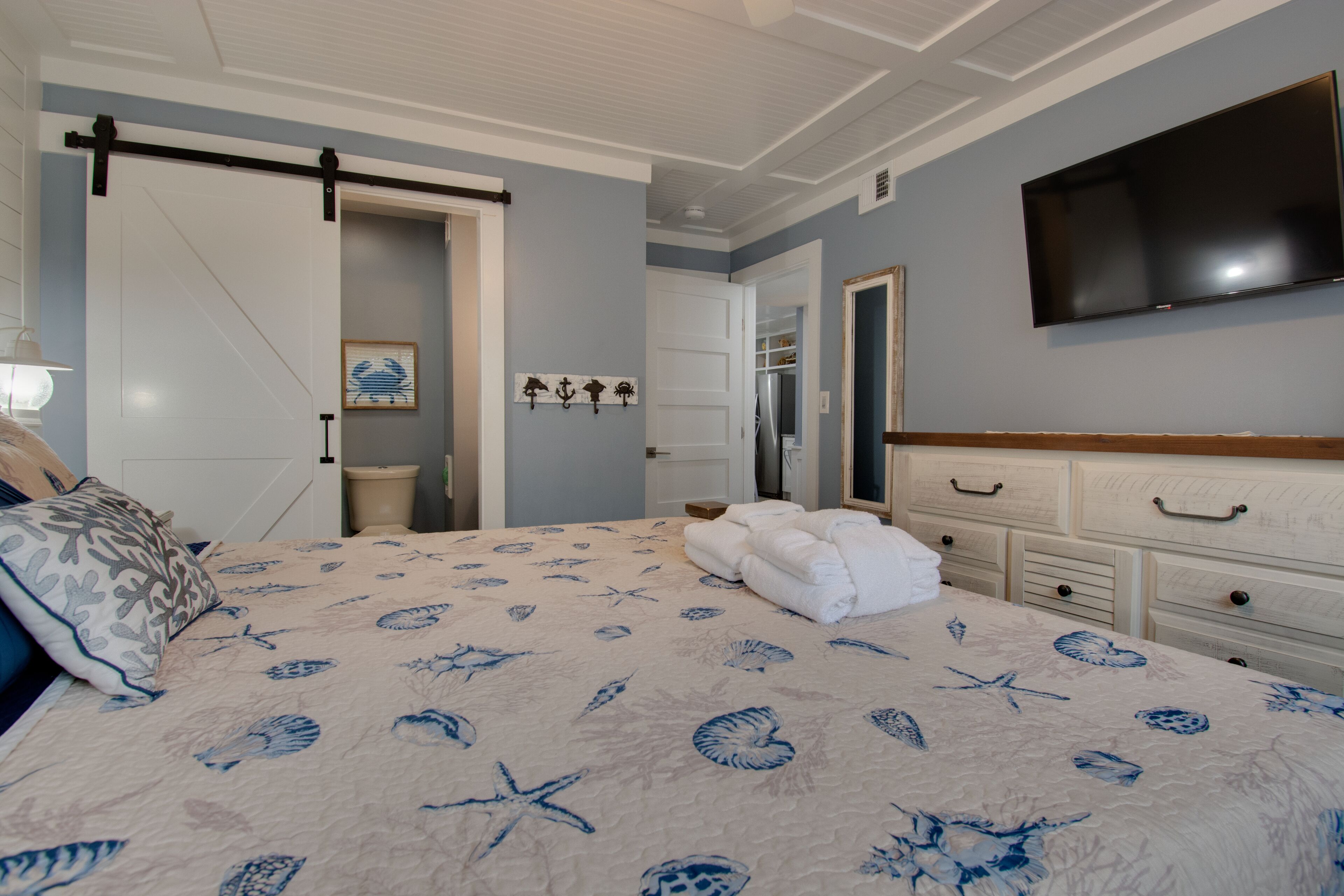 A bedroom with a bed, a TV, a wardrobe, and a door leading to a bathroom.