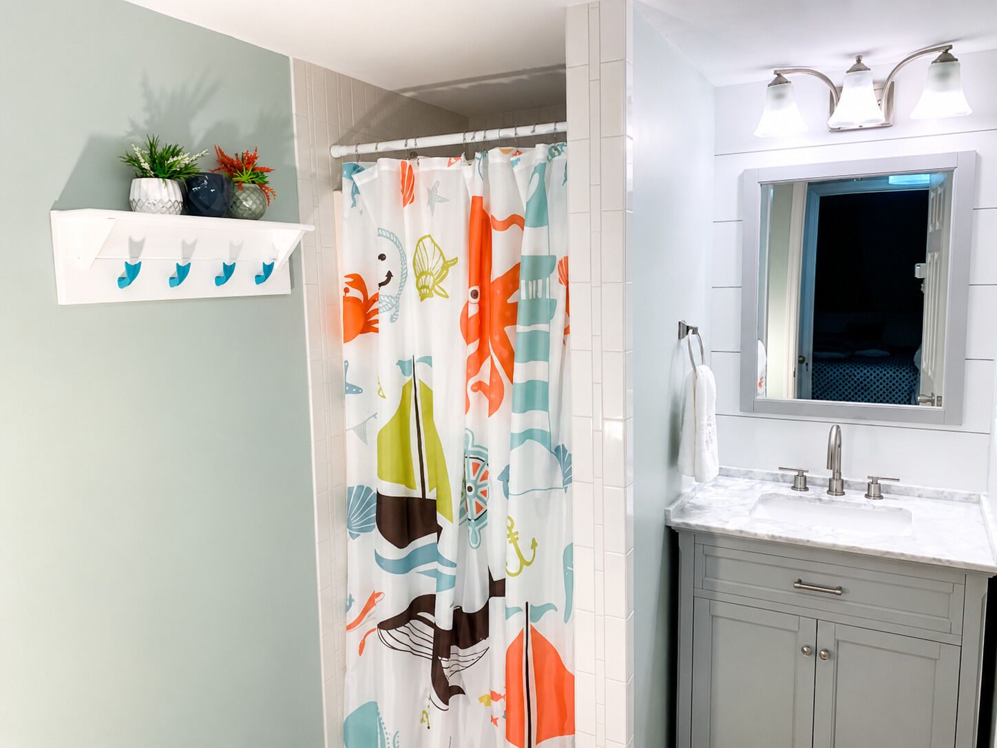 A bathroom with a shower curtain featuring a nautical theme, a white sink with a mirror above it, and a towel rack.