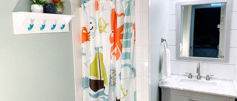A bathroom with a shower curtain featuring a nautical theme, a white sink with a mirror above it, and a towel rack.