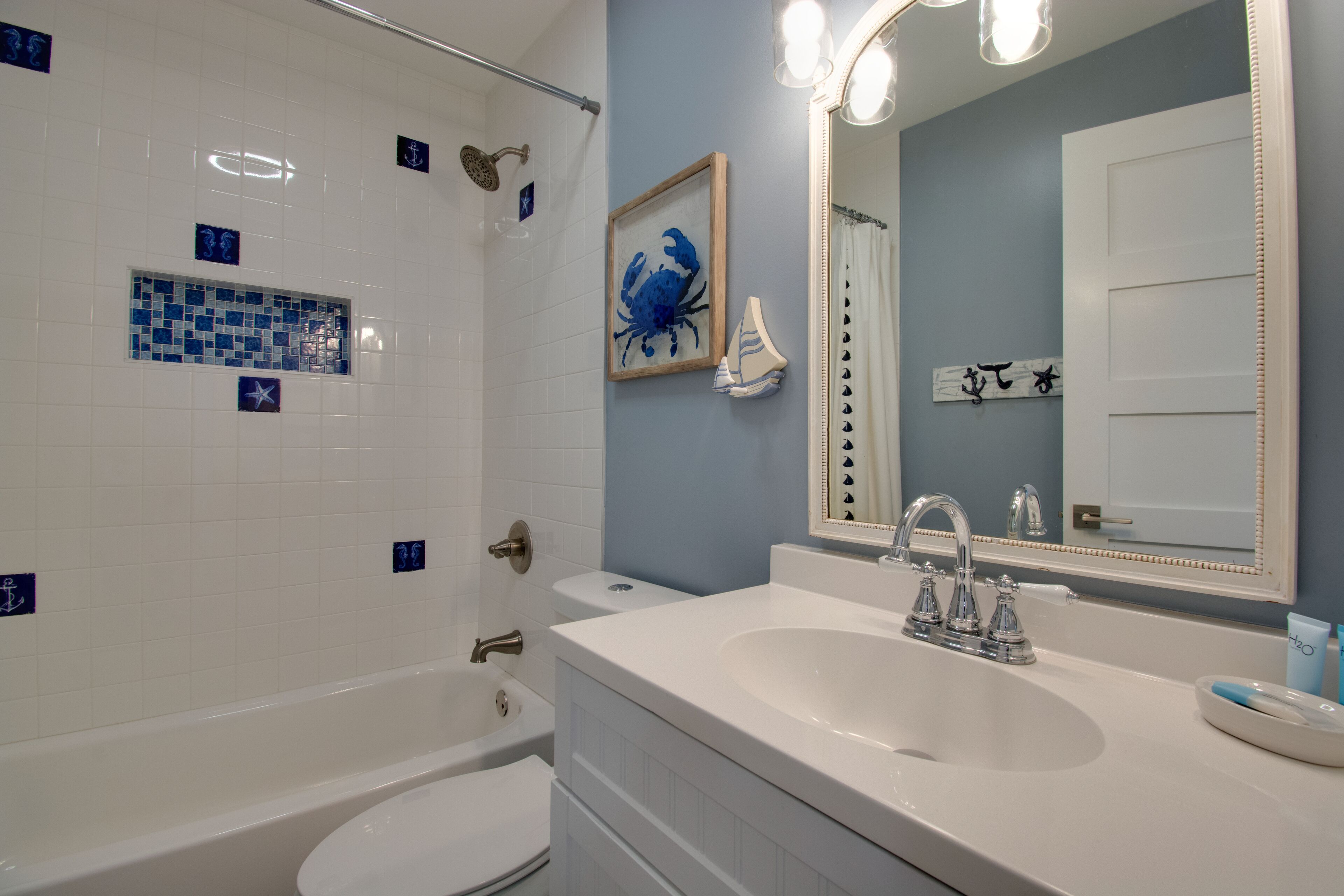 Une salle de bain avec une baignoire blanche, un lavabo et une douche. Le mur est décoré de carreaux et un tableau encadré est accroché au-dessus du lavabo.