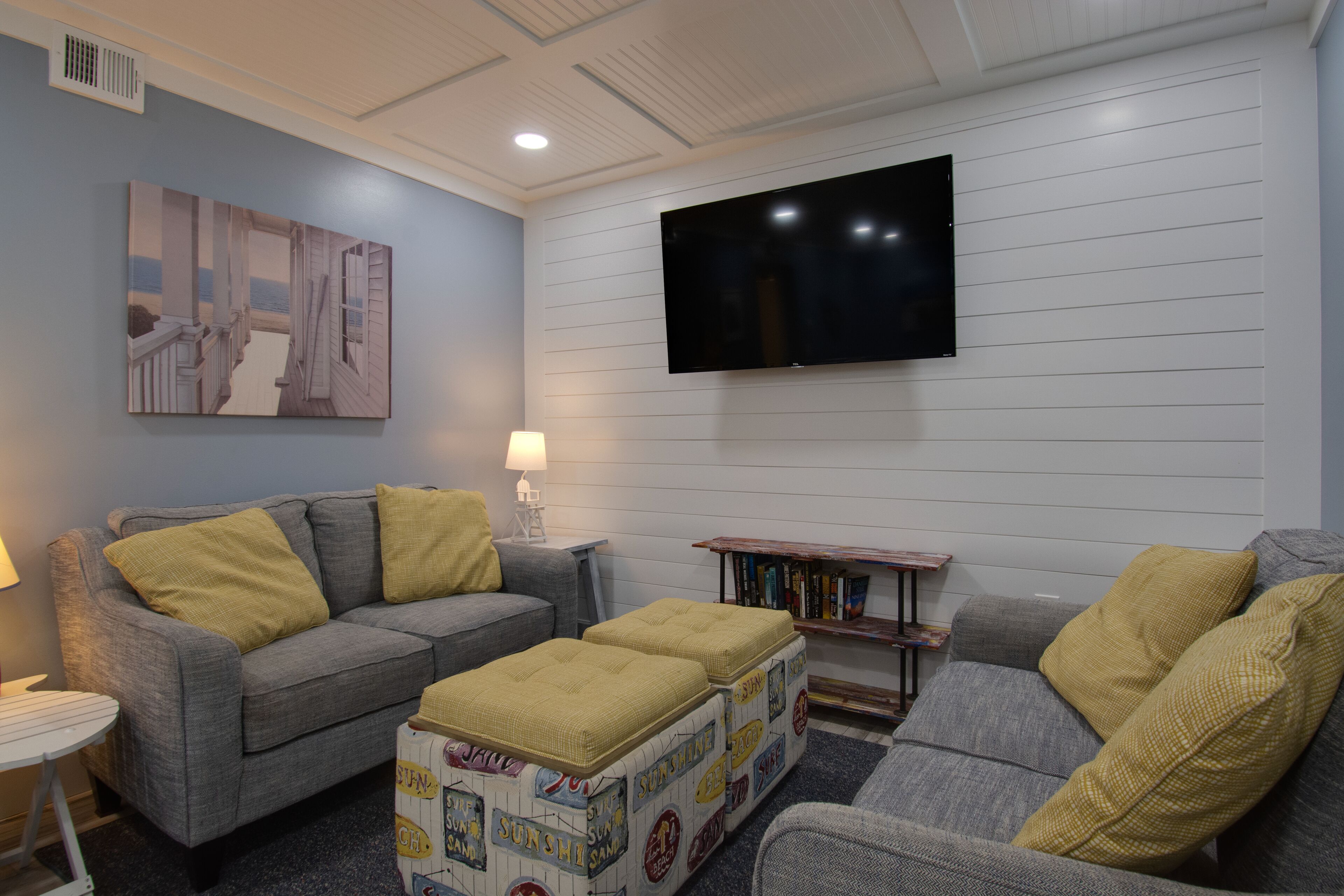 A living room with a grey sofa, a coffee table, a television mounted on the wall, and a bookshelf.