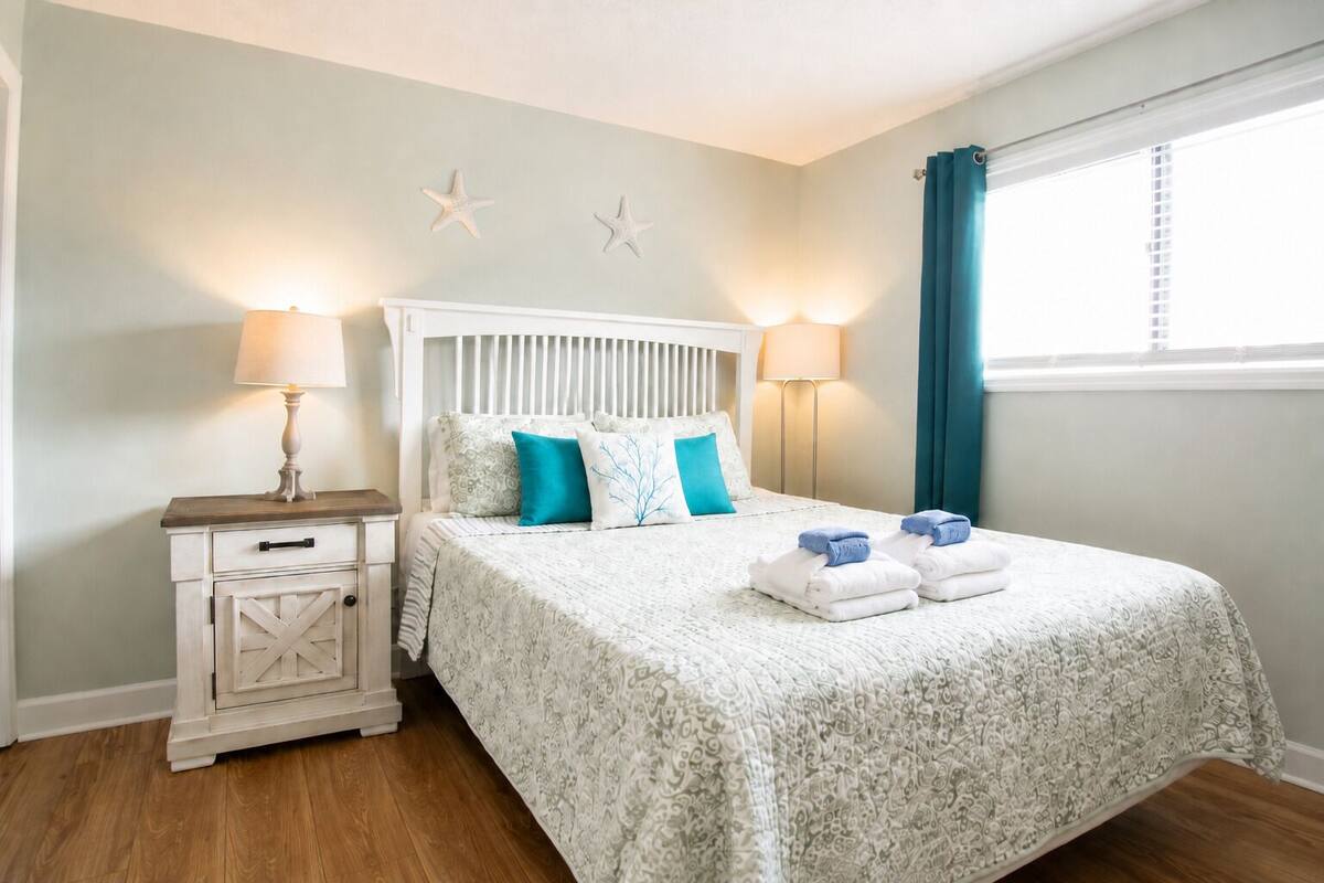 A neatly arranged bedroom with a bed, bedside tables, and a window with curtains.