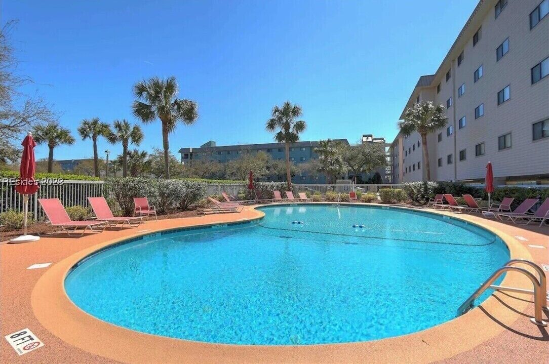 A swimming pool with lounge chairs and palm trees, surrounded by a building with multiple windows.