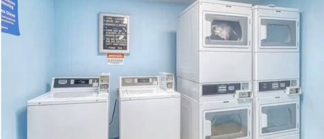 Een wasserette met gestapelde wasmachines en drogers, een prikbord en een blauwe muur.