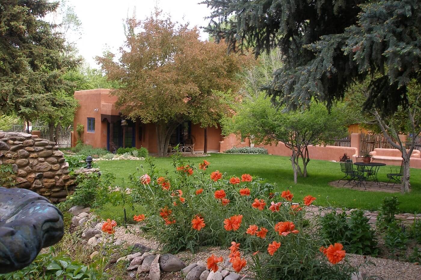 A courtyard with a stone wall, a building with a red facade, and a garden with orange flowers.