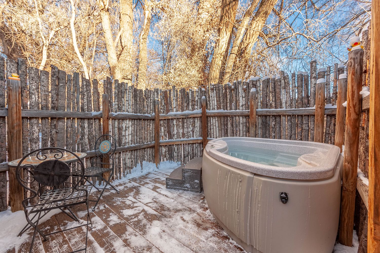 Eine Holzterrasse mit Whirlpool, Metallstühlen und einem rustikalen Zaun.