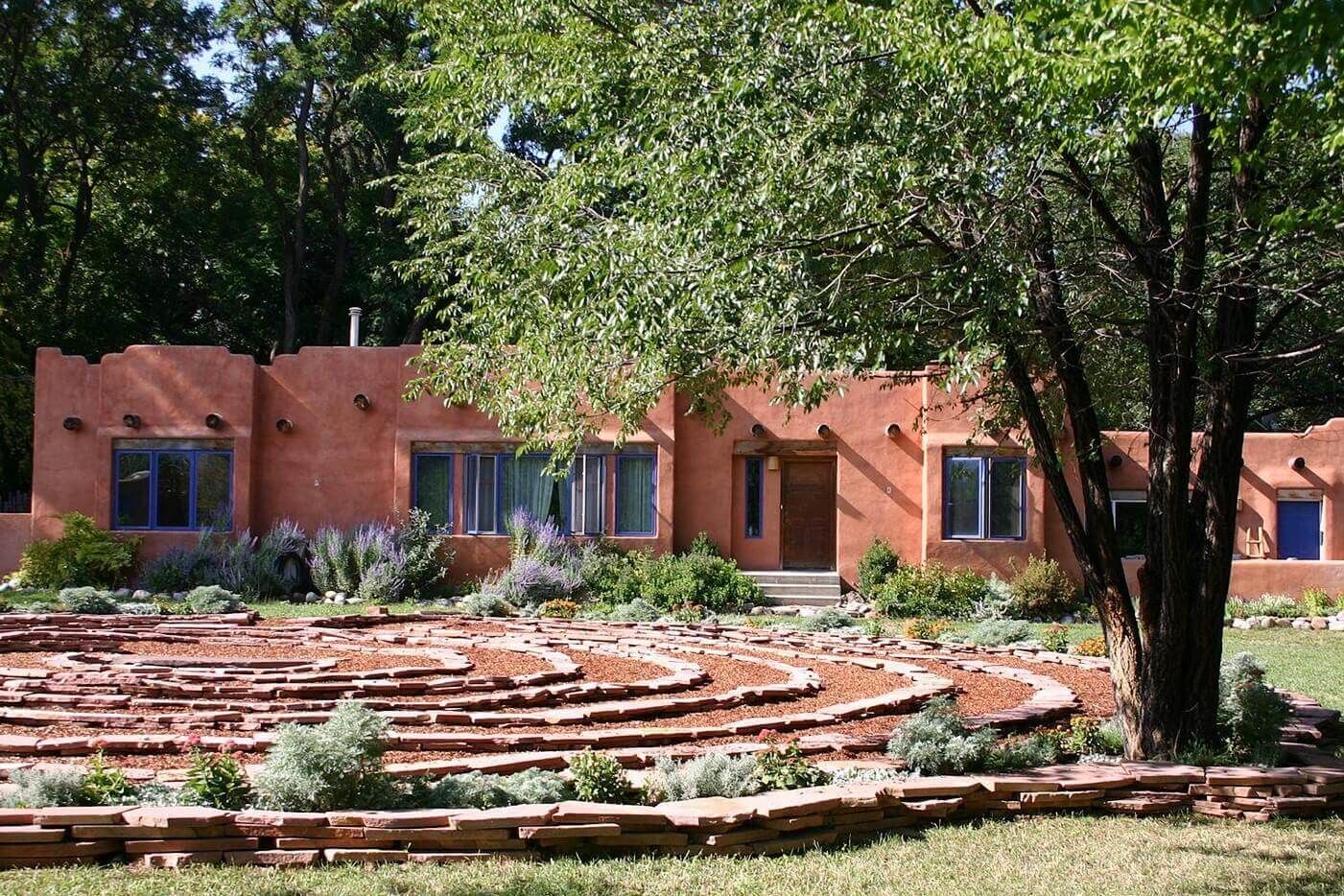 Um edifício com fachada em terracota, um jardim circular com pedras e uma árvore em primeiro plano.
