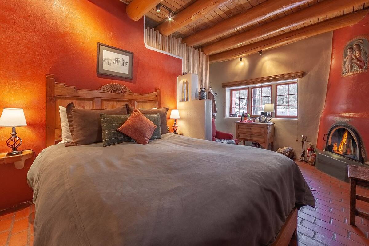 A cozy bedroom with a large bed, a fireplace, and a window with a view of trees.