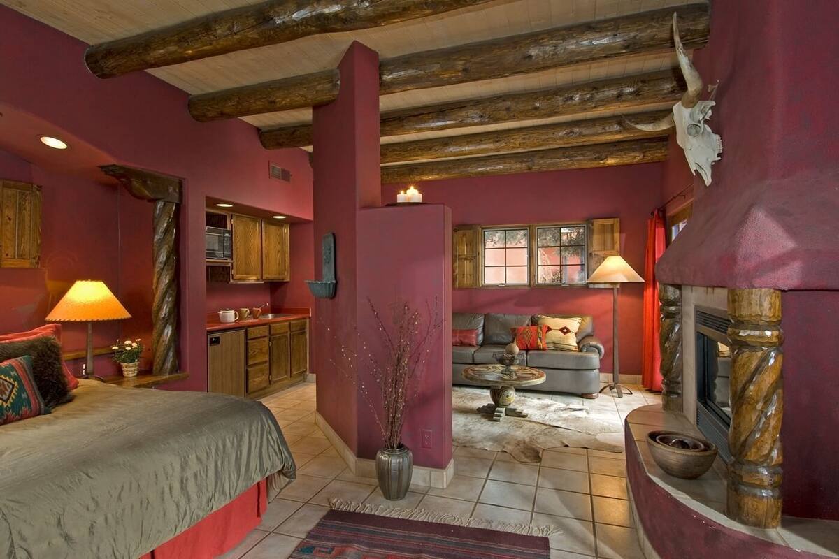 A cozy room with a bed, a sofa, a fireplace, and a kitchen area.