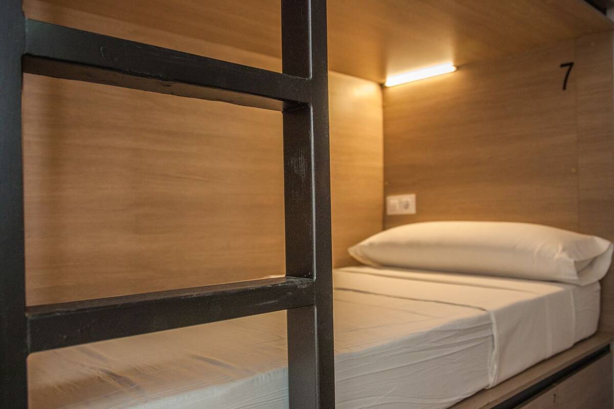 A bunk bed with a wooden frame and a mattress with white bedding.