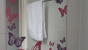 A bathroom with a mirror decorated with butterfly cutouts and a sign encouraging to love our earth and save energy. - Maindee Guest House (Barrow-in-Furness)