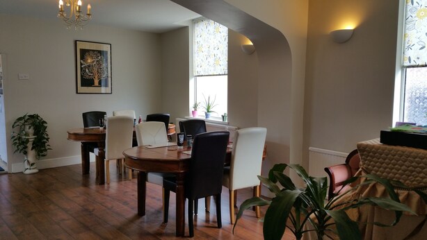 A dining area with a wooden table and chairs, a chandelier, and a framed artwork on the wall. - Maindee Guest House (Barrow-in-Furness)
