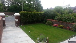 A well-maintained garden with a paved pathway leading to a gated entrance, surrounded by lush greenery and flowering plants. - Maindee Guest House (Barrow-in-Furness)