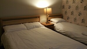 A room with two single beds, wooden headboards, a nightstand with a lamp, and a wall with a birdcage pattern. - Maindee Guest House (Barrow-in-Furness)