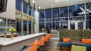 A modern bar area with a long counter, multiple orange bar stools, and a seating area with a sofa and chairs.