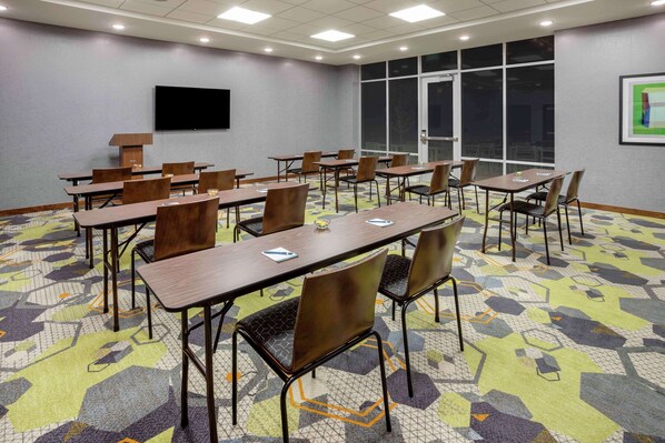 Un salón de conferencias con varias mesas y sillas, una pantalla grande y un ventanal con vistas.