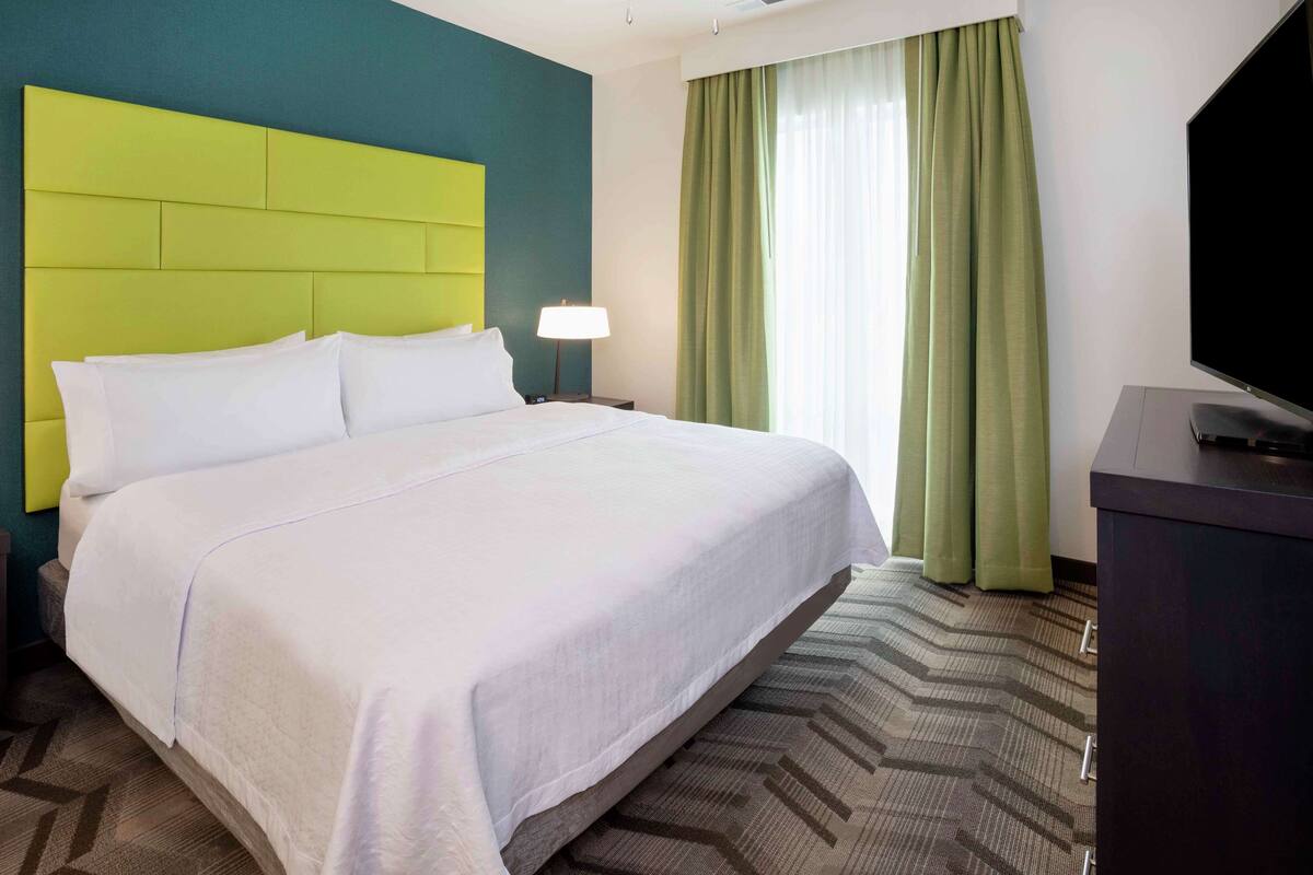 A hotel room with a large bed, a flat-screen TV, a nightstand, and a lamp.