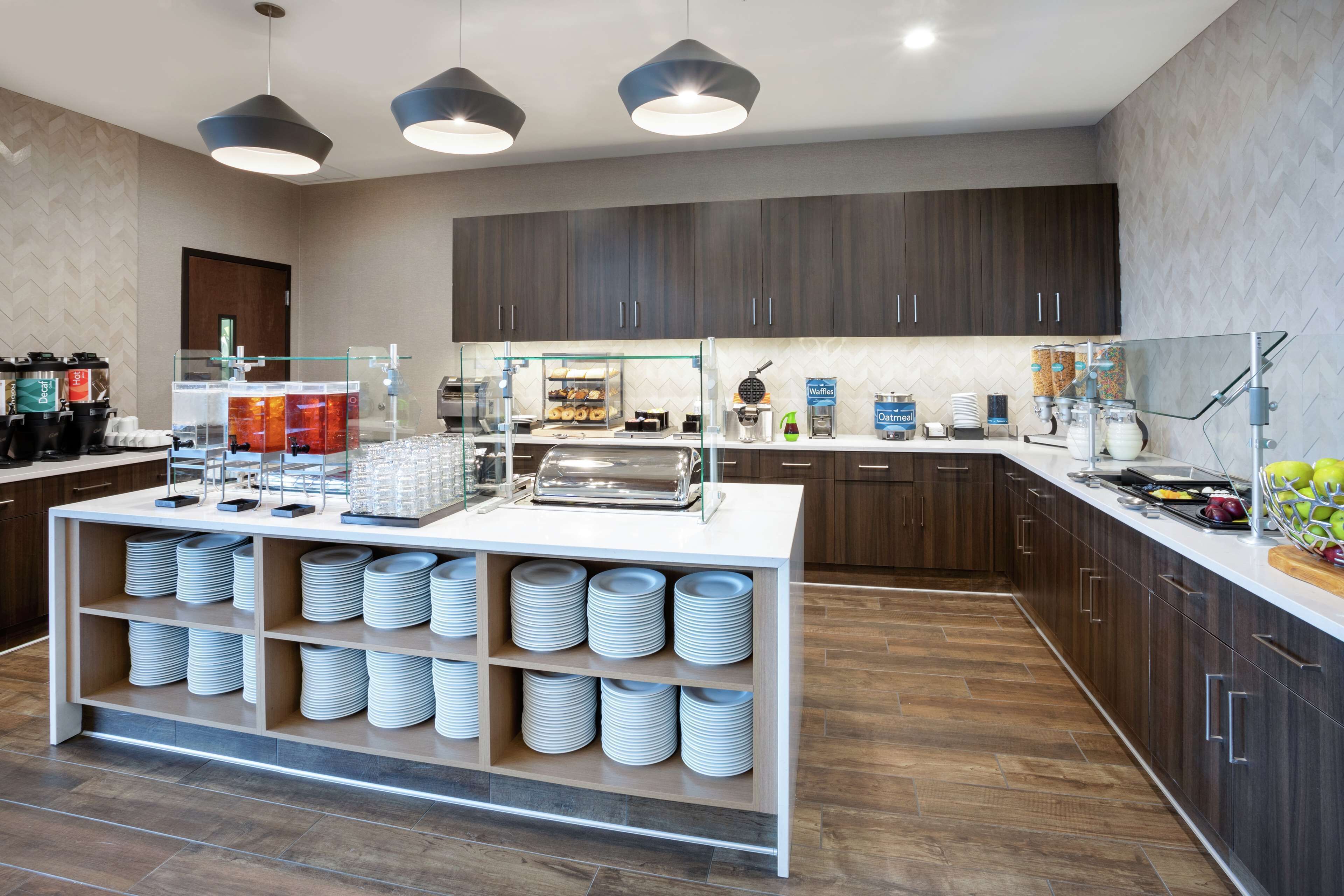 A modern kitchen with a buffet setup, including a glass display case, a coffee station, and a variety of food items.