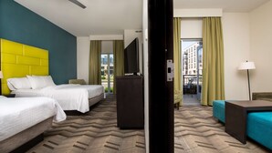 A hotel room with two beds, a television, a desk, and a view of the city.