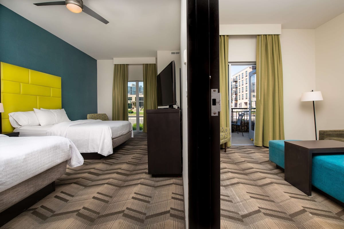 A hotel room with two beds, a television, a desk, and a view of the city.