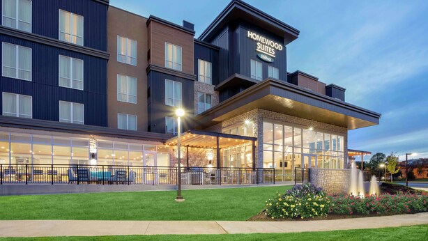 A hotel with a modern design, featuring a covered outdoor seating area and a landscaped garden.
