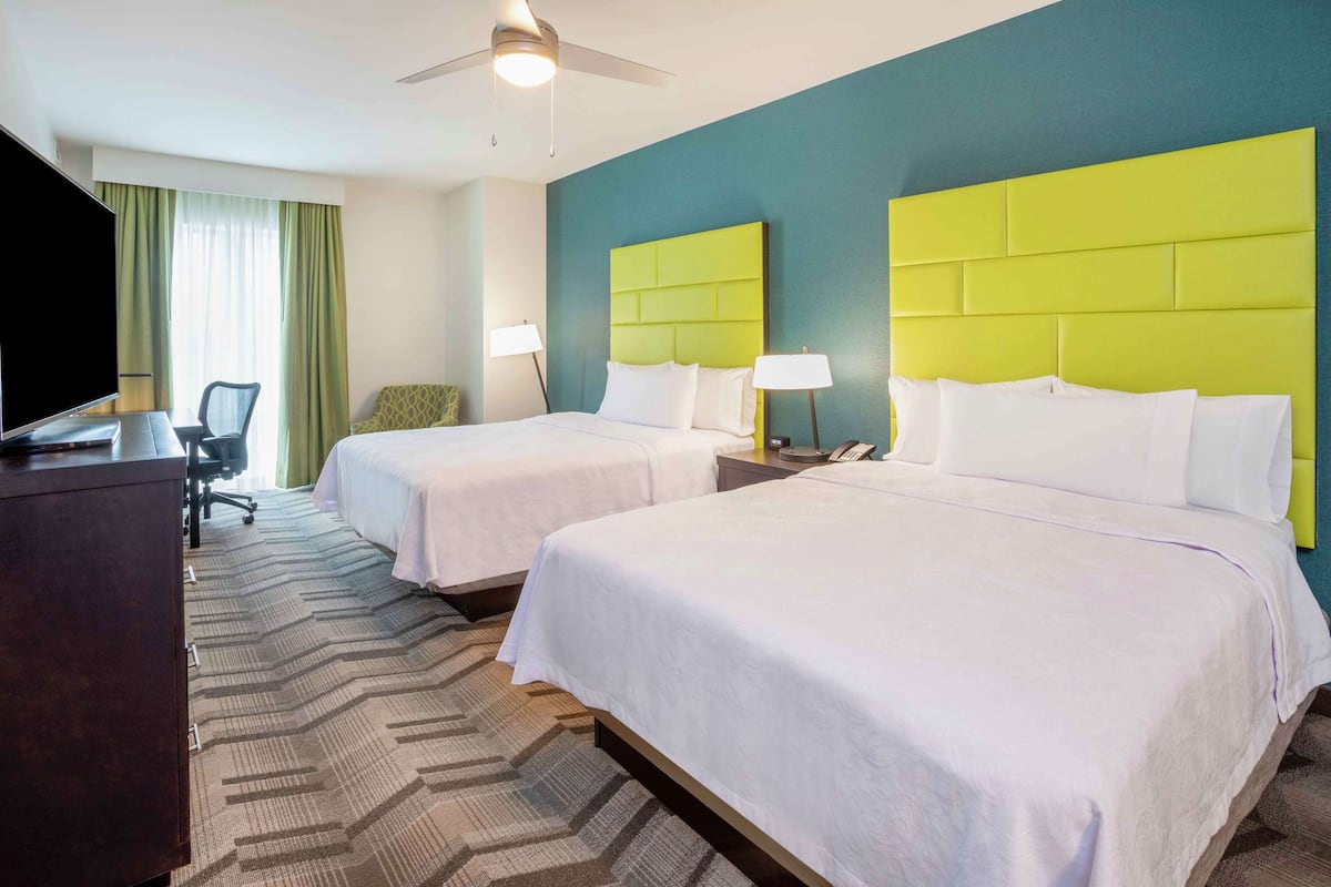 A hotel room with two beds, a desk, a TV, and a ceiling fan.