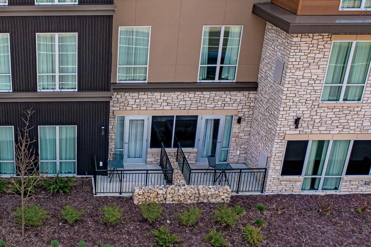 A multi-story building with a stone facade, multiple windows with curtains, and a small outdoor seating area with a stone bench.