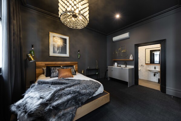 A modern bedroom with a large bed, a chandelier, a bedside table, a mirror, and a bathroom with a sink and mirror.