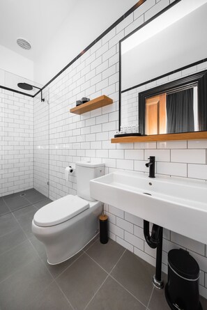 A modern bathroom with white subway tiles, a white toilet, a black sink, and a shower area.