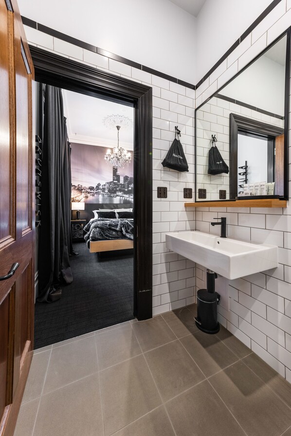Un baño moderno con un lavamanos blanco, un cubo de basura negro y un espejo encima.