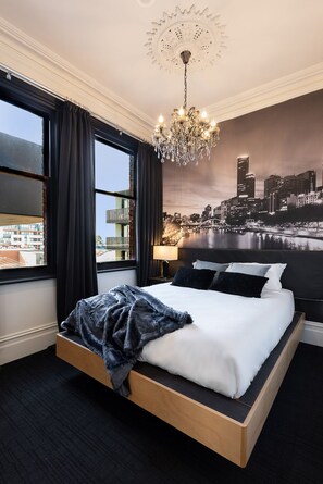 Una habitación de hotel moderna con una cama grande, una araña y un mural de paisaje urbano en la pared.