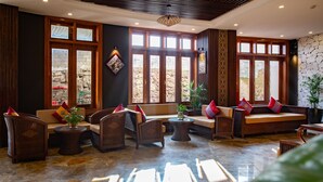 A spacious lobby with multiple seating areas, large windows, and a stone wall. - The View Sapa Hotel (Sa Pa)