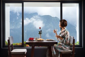 A person seated at a table with a view of mountains through a large window. - The View Sapa Hotel (Sa Pa)