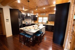A modern kitchen with wooden ceiling, dark cabinets, a central island with stools, and a 'FAMILY' sign. - Wolf Lodge overlooking Lake Petenwell Fireplace, Firepit, Full Arcade. (Necedah)