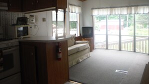 Cocina equipada con microondas, estufa y alacenas. Hay un televisor sobre un soporte y una ventana con cortinas.