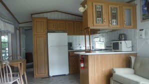 Una cocina compacta con armarios de madera, un refrigerador, un microondas y una zona de comedor con una mesa y sillas.