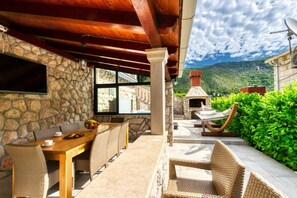 An outdoor patio with stone walls, a wooden table, wicker chairs, a hammock, and a stone fireplace. - Family Friendly Home with Private Heated Pool & Basketball Court (Dubrovnik)