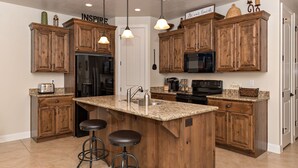Una cocina con armarios de madera, encimera de granito, refrigerador, microondas y cafetera.