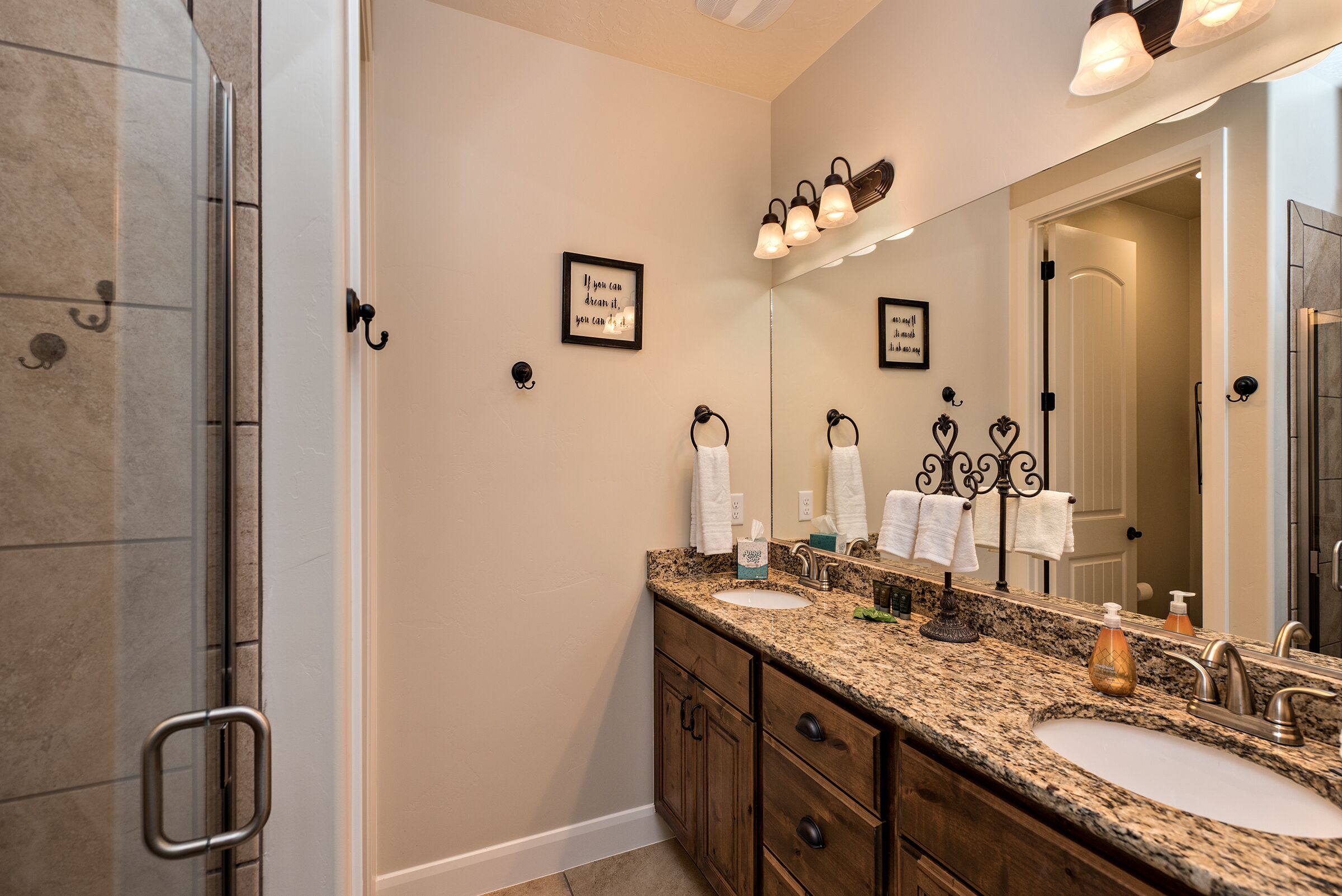 A bathroom with a granite countertop, two sinks, a large mirror, and a shower area.