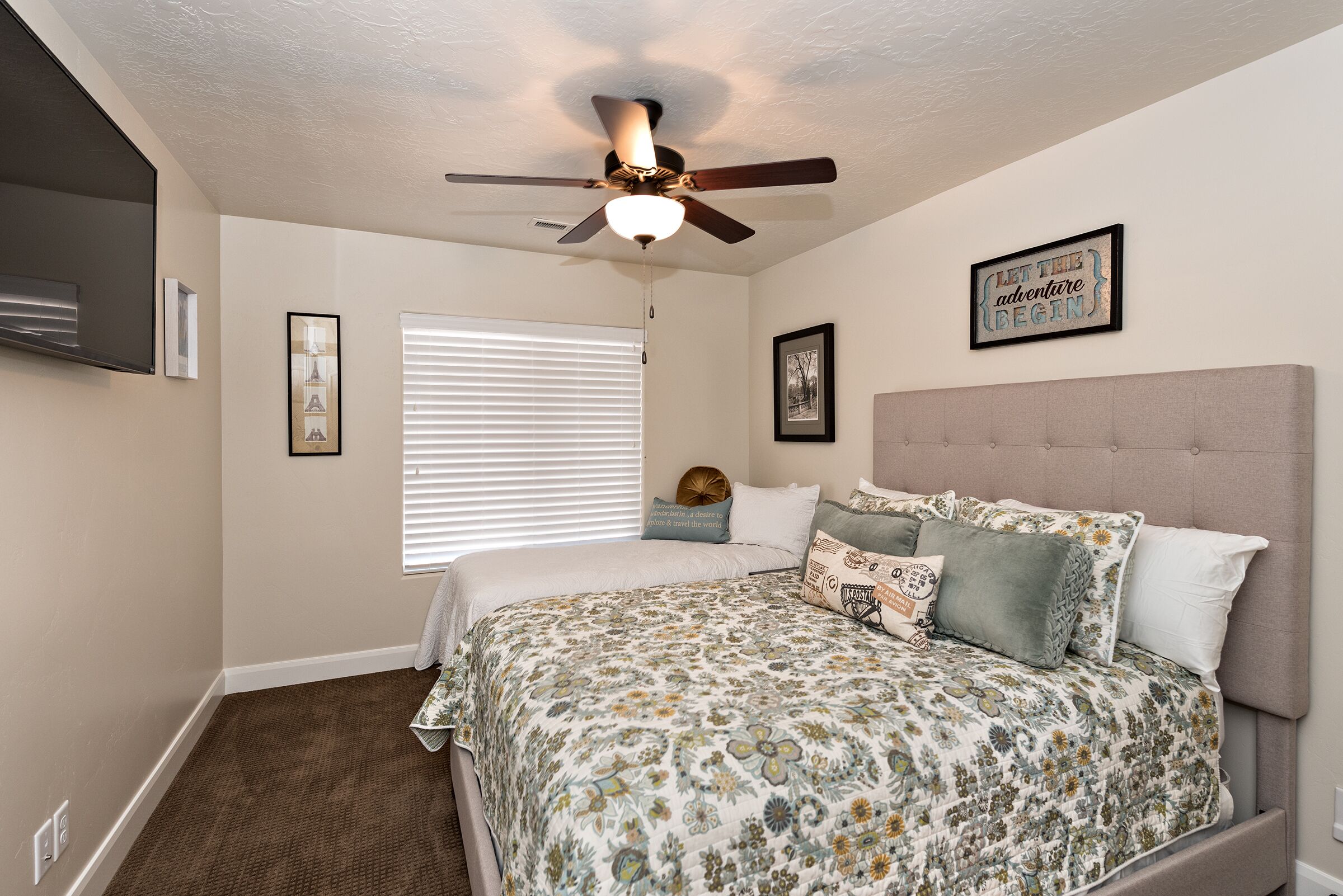 A bedroom with a bed, a ceiling fan, a window with blinds, and a motivational quote on the wall.