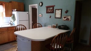 A kitchen with wooden cabinets, a white refrigerator, a built-in dishwasher, and a dining table with four chairs. There are wall decorations and a clock on the wall.