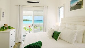 Un dormitorio con una cama grande, cortinas blancas, vista al océano y un balcón con mesa y sillas.