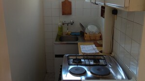 Cocina compacta con estufa a gas, un lavamanos y una ventana sobre la encimera.