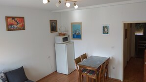 Un espacio habitable compacto con zona de comedor, microondas sobre un refrigerador pequeño y sofá con manta.