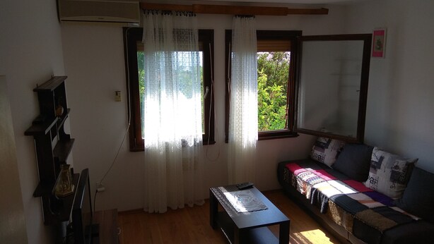 Una sala de estar con piso de madera, un sofá con una manta colorida, una mesita de centro y un estante montado en la pared.