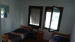 Una habitación pequeña y poco amueblada con dos camas de madera, una mesita y una ventana con persianas.